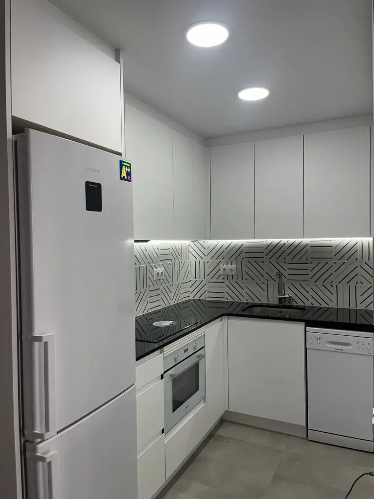 Cocina blanca sin tiradores con frontal geométrico y luz LED bajo muebles